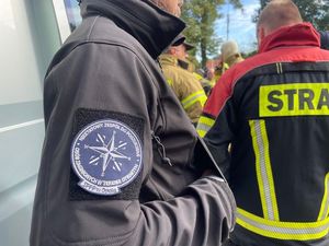 Zdjęcie w kolorze przedstawia kilka umundurowanych osób, NA pierwszym planie mężczyzna z emblematem Grupy poszukiwawczej.