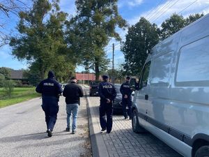 Zdjęcie w kolorze przedstawia policjantów oraz osoby cywilne idące po jezdni. Na pierwszym planie po prawej stronie Pojazd typu Bus w kolorze metalik.