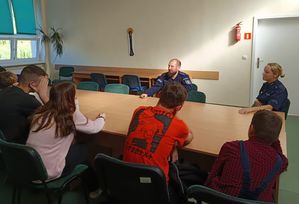 Zdjęcie w kolorze przedstawia policjantów siedzących w klasie z uczniami przy złączonych stołach.