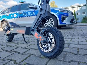 Zdjęcie w kolorze przedstawia hulajnogę elektryczną na tle radiowozu.