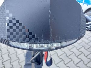 Zdjęcie w kolorze przedstawia lampę przednia hulajnogi elektrycznej z widocznymi uszkodzeniami -  otarciem.