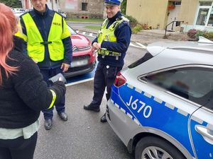 Zdjęcie w kolorze przedstawia jak policjanci wręczają mężczyźnie i kobiecie odblaski.