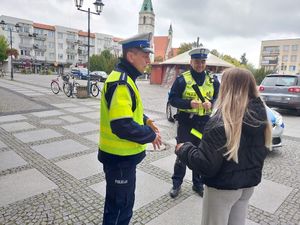 Zdjęcie w kolorze przedstawia jak policjanci wręczają kobiecie odblask.