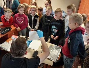 Zdjęcie w kolorze przedstawia grupę dzieci w pomieszczeniu technika kryminalistyki podczas pokazu wyposazenia i utrwalania sladów.