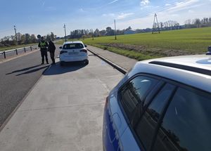 Zdjęcie w kolorze przedstawia policjanta dokonuącego kontroli pojazdu osobowego.