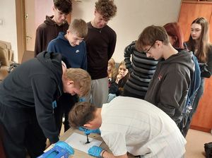 Zdjęcie w kolorze przedstawia młodzież podczas zajęć w pracowni technika kryminalistyki. Uczniowie sami wykonują odbitki palców.