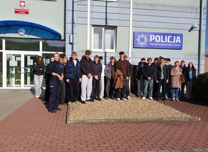 Zdjęcie w kolorze przedstawia grupę młodzieży pozująca do zdjęcia z policjantka przed budynkiem KPP w Oleśnie.