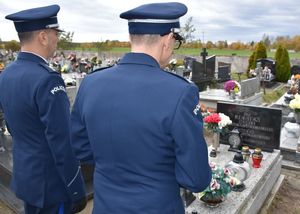 Zdjęcie w kolorze przedstawia dwóch policjantów w mundurach galowych stojących przy grobie, w tle inne mogiły.