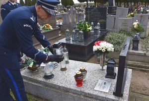 Zdjęcie w kolorze, przedstawia policjanta w mundurze galowym, który pochyla się nad płyta nagrobkowa odkładając na nią znicz.