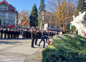 Zdjęcie w kolorze przedstawia delegację służb mundurowych z komendantem powiatowym policji, który składa kwiaty pod pomnikiem.