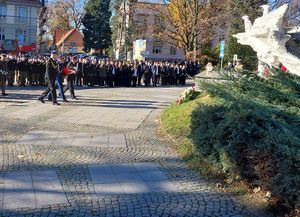 Zdjęcie w kolorze przedstawia przedstawicieli służb w idących złożyć kwiaty pod pomnikiem.