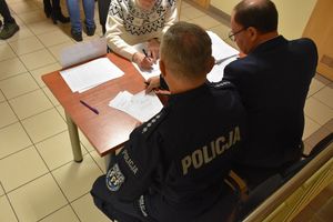 Zdjęcie w kolorze przedstawia punkt kontrolno informacyjny przy którym siedzi policjant i pracownik cywilny.