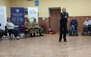 Zdjęcie w kolorze, przedstawia policjantkę stojącą pośrodku sali, do koła niej uczestnicy spotkania.