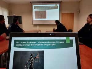 Zdjęcie w kolorze przedstawia na pierwszym planie ekran laptopa na nim wyświetlony slajd zawierający napis : Akty prawa krajowego i międzynarodowego dotyczące zasady równego traktowania ze względu na płeć.