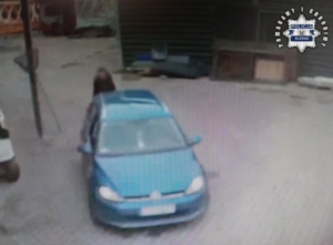 Zdjęcie w kolorze przedstawia kadr z monitoringu zewnętrznego na którym stoi zaparkowany niebieski pojazd osobowy z tyłu za pojazdem stoi mężczyzna. Obraz jest pozbawiony ostrości.