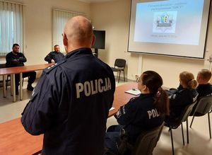 Zdjęcie w kolorze przedstawia policjantów podczas odprawy w sali odpraw, spoglądają na ekran ze slajdem z napisami Plan Ćwiczenia Dowódczo-Sztabowego pod kryptonimem Obcy