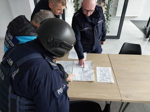 Zdjęcie w kolorze przedstawia policjantów zapoznających się z planami budynku.