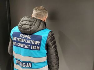 Zdjęcie w kolorze przedstawia policjanta Zespołu antykonfliktowego stojącego przy drzwiach koloru grafitowego.