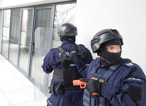 Zdjęcie w kolorze przedstawia policjantów w hełmach idących po balkonie.