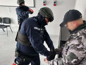 Zdjęcie w kolorze przedstawia policjantów w hełmach i kominiarkach podczas zatrzymania mężczyzny.