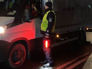 Zdjęcie w kolorze przedstawia policjanta z świecącym na czerwono sygnalizatorem prowadzi kontrolę trzeźwości kierującego pojazdem dostawczym.