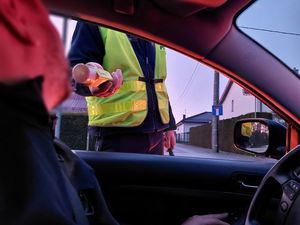 Zdjęcie w kolorze przedstawia scenę z wnętrza pojazdu jak policjant podaje urządzenie do dmuchania kierującemu.