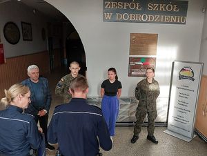 Zdjęcie w kolorze przedstawia uczniów klas mundurowych podczas wręczenia nagród na holu szkolnym.