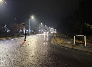 Zdjęcie w kolorze przedstawia porę nocną, na pierwszym planie  policjant na jezdni wydaje sygnał do zatrzymania kierującemu ciężarówką.