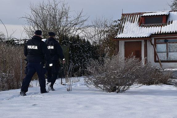 Zdjęcie w kolorze przedstawia policjantów idących w stronę altany działkowej w śnieżnej scenerii