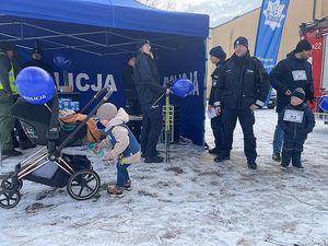 Zdjęcie w kolorze przedstawia stoisko policyjne - namiot w kolorze niebieskim z napisem policja i stojące przy nim osoby w tym kilku policjantów.