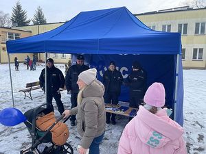 Zdjęcie w kolorze przedstawia niebieski namiot z napisem policja, przy nim kilka osób oraz policjanci, do koła śnieg.