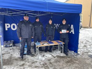 Zdjęcie w kolorze przedstawia policjantów stojących pod namiotem z napisem policja.