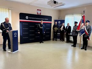 Zdjęcie w kolorze przedstawia uroczystą zbiórkę z udziałem pocztu sztandarowego KPP w Oleśnie , Komendant stoi przy mównicy.