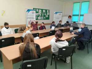 Zdjęcie w kolorze przedstawia uczniów siedzących przy podłużnym stole na przeciw nich siedzi policjant.