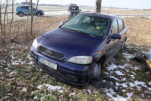 Zdjęcie w kolorze przedstawia granatowego opla, zaparkowanego na obszarze rolniczym, w tle jezdnia na której stoją dwa inne samochody.