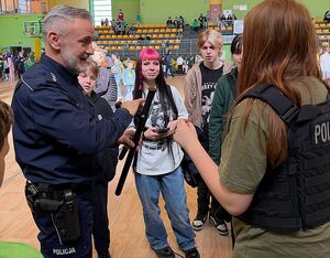 Zdjęcie w kolorze przedstawia policjanta demonstrującego młodzieży pałkę tonfa.