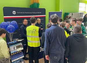 Zdjęcie w kolorze przedstawia kilkanaście osób zgromadzonych przed stoiskiem promocyjnym policjantów.