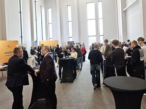 Zdjęcie w kolorze przedstawia uczestników konferencji zgromadzonych na sali ze stoiskami promocyjnymi.