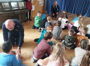 Zdjęcie w kolorze, przedstawia   przedszkolaków  ćwiczących czynności resuscytacji na maskotkach. Pokazu udzielają policjant  i policjantka.