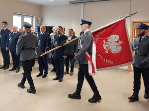 Zdjęcie w kolorze przedstawia poczet sztandarowy wstępujący  podczas rozpoczęcia uroczystości w tle zgromadzeni goście.