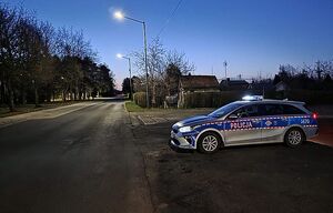 Zdjęcie w kolorze przedstawia radiowóz stojący prostopadle do jezdni, bardzo wczesny świt.