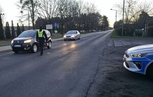 Zdjęcie w kolorze przedstawia policjanta stojącego przy pojeździe na jezdni podczas kontroli trzeźwości.
