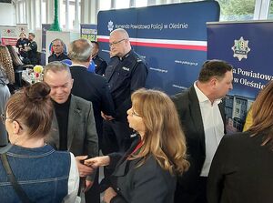 Zdjęcie w kolorze przedstawia policjantów rozmawiających z uczestnikami targów pracy na tle  ściany z płótna z napisem Komenda Powiatowa Policji w Oleśnie.