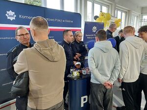 Zdjęcie w kolorze przedstawia policjantów rozmawiających z uczestnikami targów pracy na tle  ściany z płótna z napisem Komenda Powiatowa Policji w Oleśnie.
