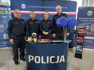 Zdjęcie w kolorze przedstawia policjantów pozujących do zdjęcia na tle  ściany z płótna z napisem Komenda Powiatowa Policji w Oleśnie.