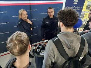 Zdjęcie w kolorze przedstawia policjantów rozmawiających z uczestnikami targów pracy na tle  ściany z płótna z napisem Komenda Powiatowa Policji w Oleśnie.