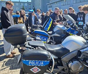 Zdjęcie w kolorze przedstawia uczniów liceum na policyjnym placu zewnętrznym podczas demonstracji pojazdów.