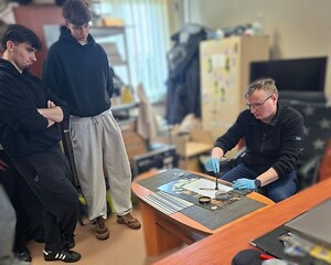 Zdjęcie w kolorze przedstawia uczniów liceum podczas zajęć z technikiem kryminalistyki, który demonstruje metody utrwalania śladów.