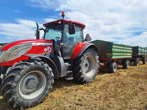 Zdjęcie w kolorze przedstawia czerwony traktor z przyczepami na polu