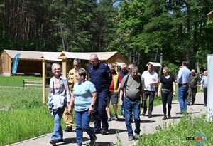 Zdjęcie w kolorze przedstawia uczestników wydarzenia podczas przemarszu w obszarze leśnym.